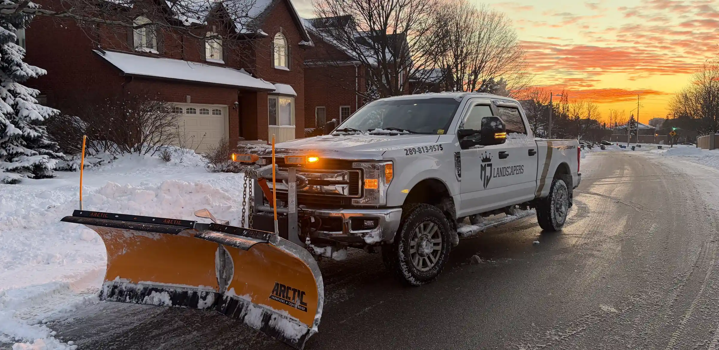 MJ Landscapers plow truck on a residential street at sunset