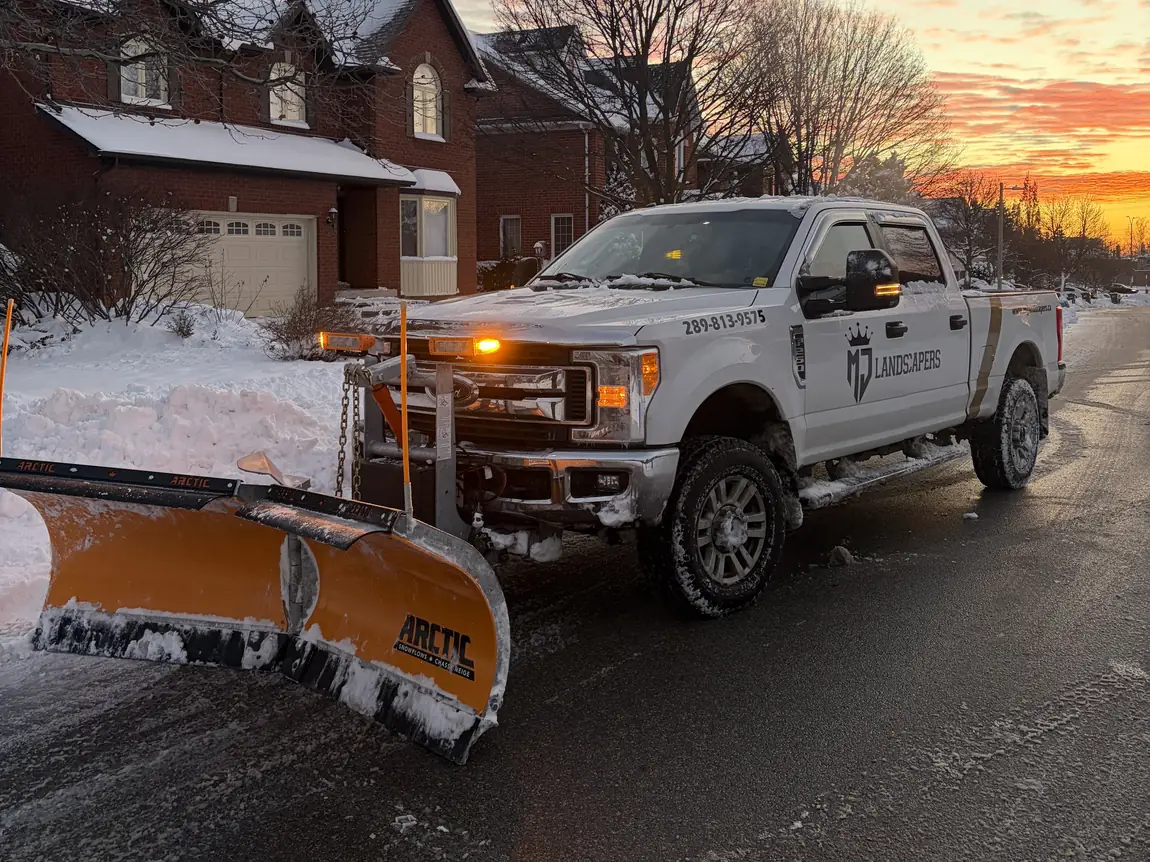 MJ Landscapers plow truck clearing a residential street at sunset